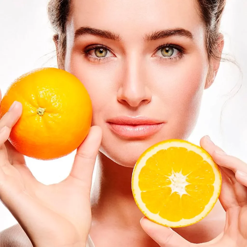 Mujer hermosa piel blanca con una naranja completa y otra partida mostrando vitamina C